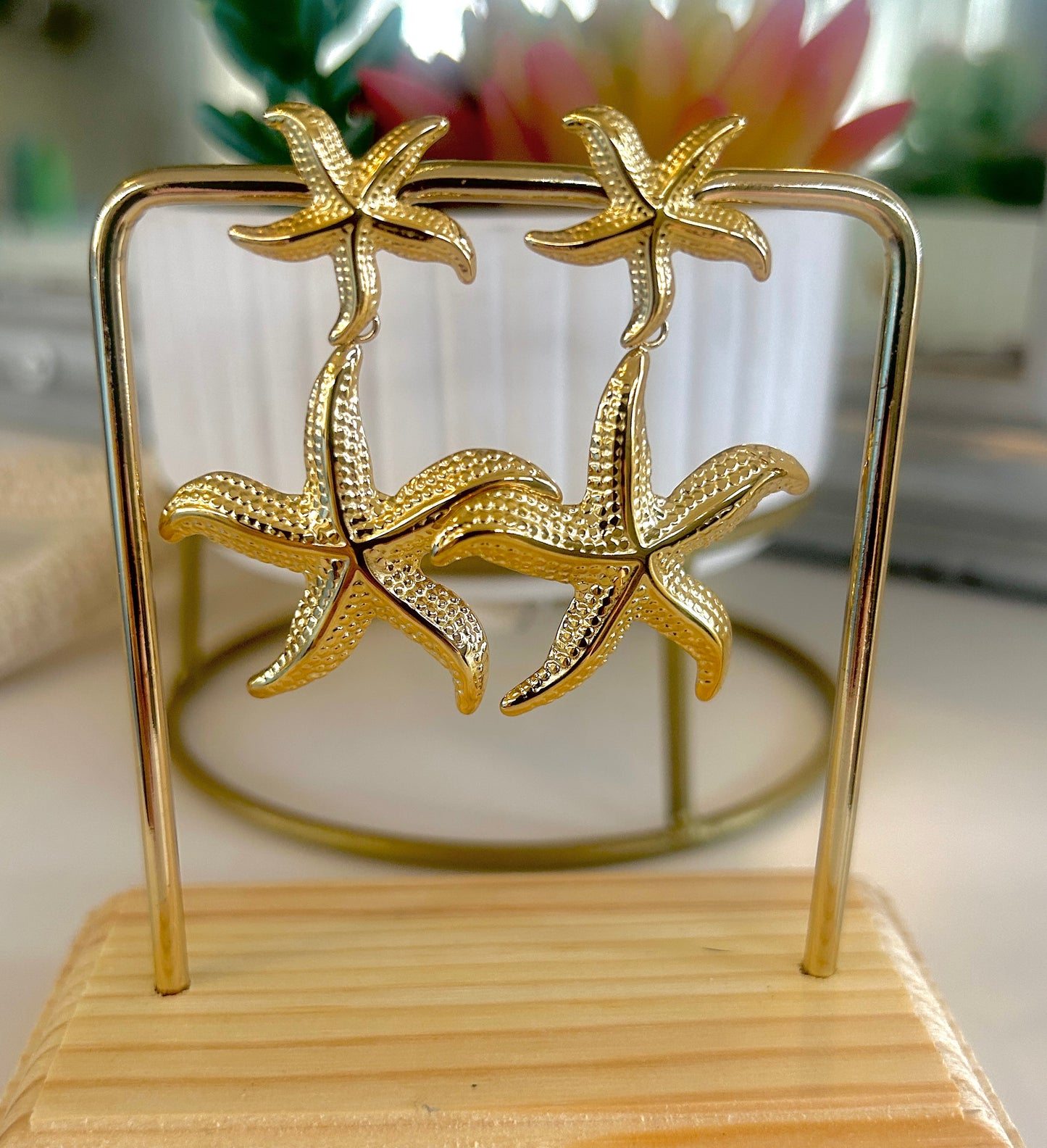 Gold starfish earrings on a stand with a blurred background