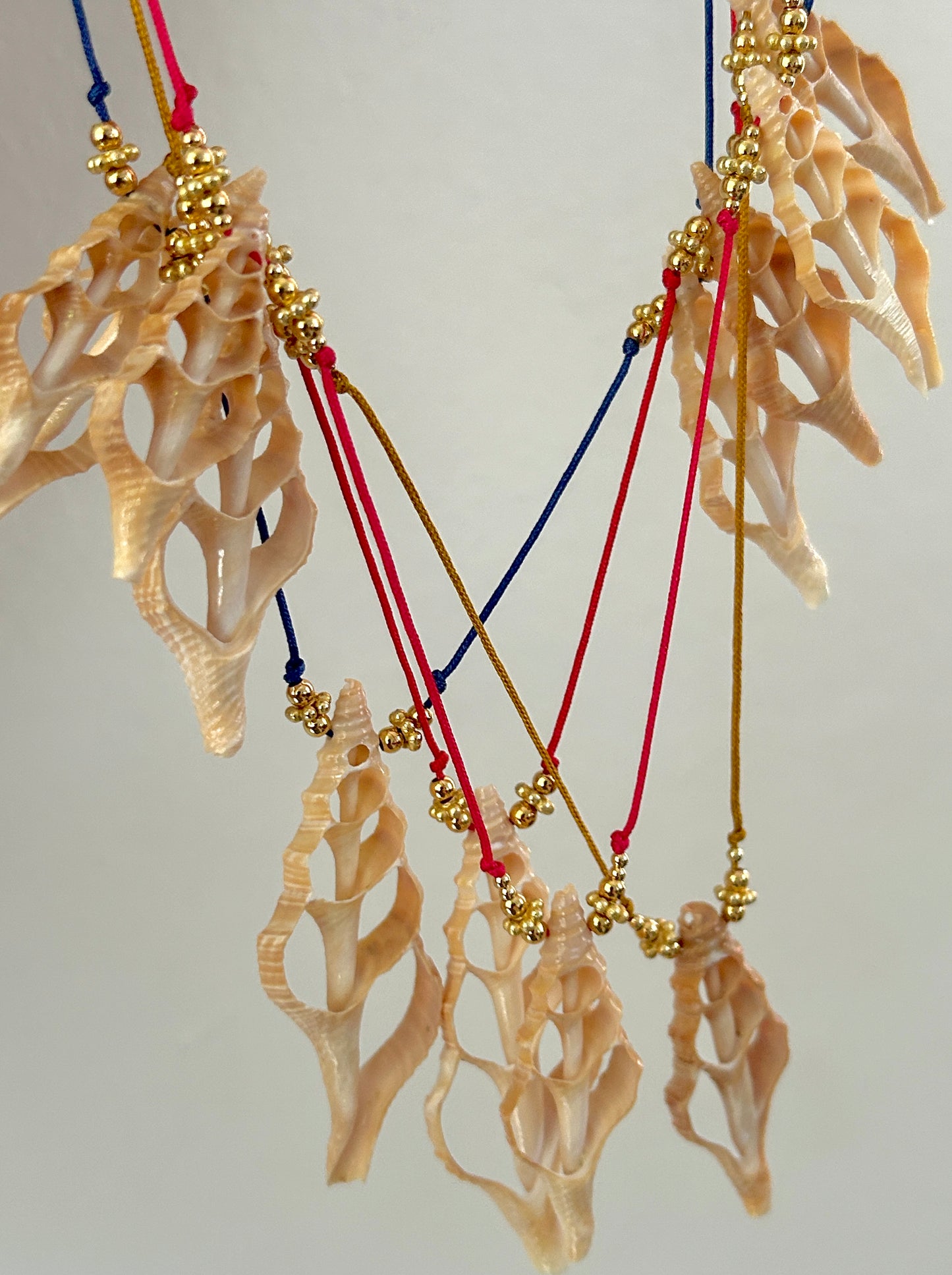 Decorative hanging with shell-like elements and colorful strings on a plain background