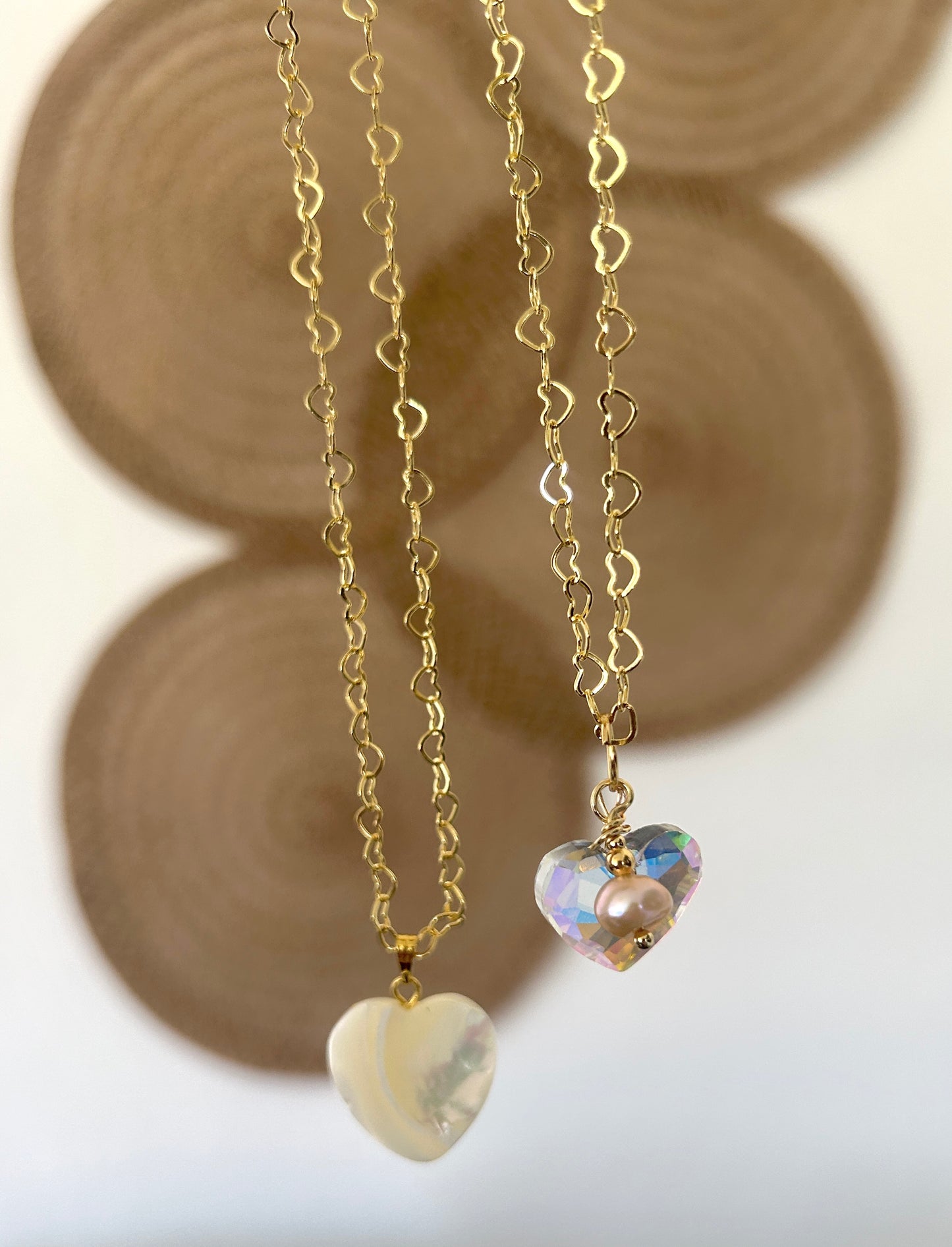 Two heart-shaped pendants on gold chains with a blurred background
