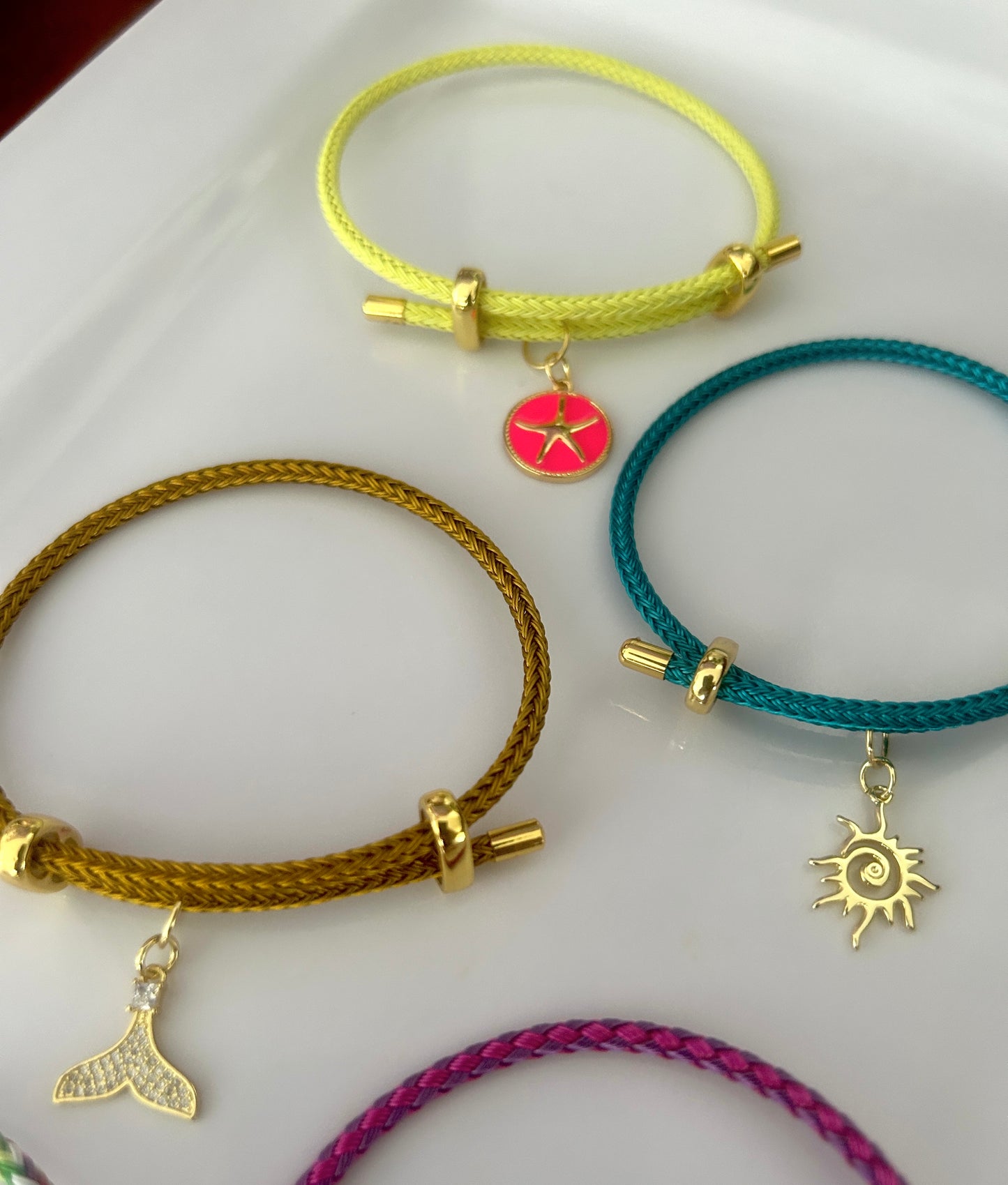 Four colorful bracelets with charms on a white surface