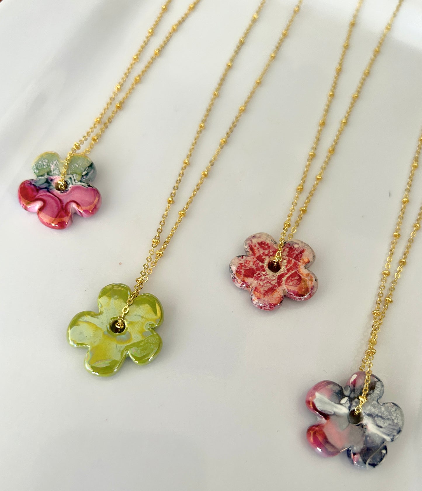 Three floral necklaces with colorful pendants on gold chains against a white background.