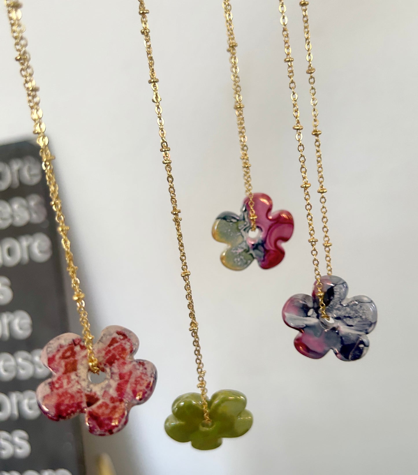 Three floral pendant necklaces on gold chains with a blurred background.