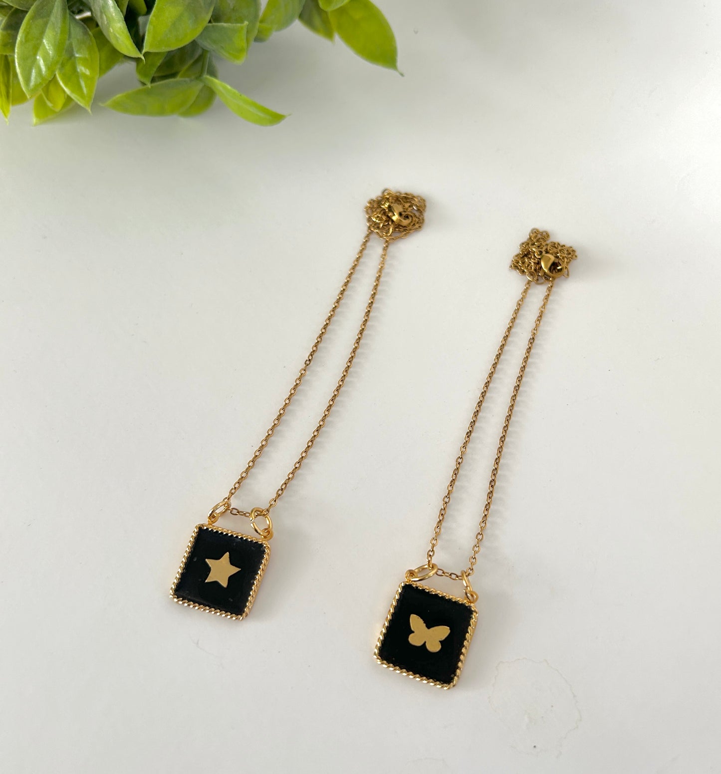 Pair of gold chain earrings with black square pendants featuring star and butterfly designs on a white background.
