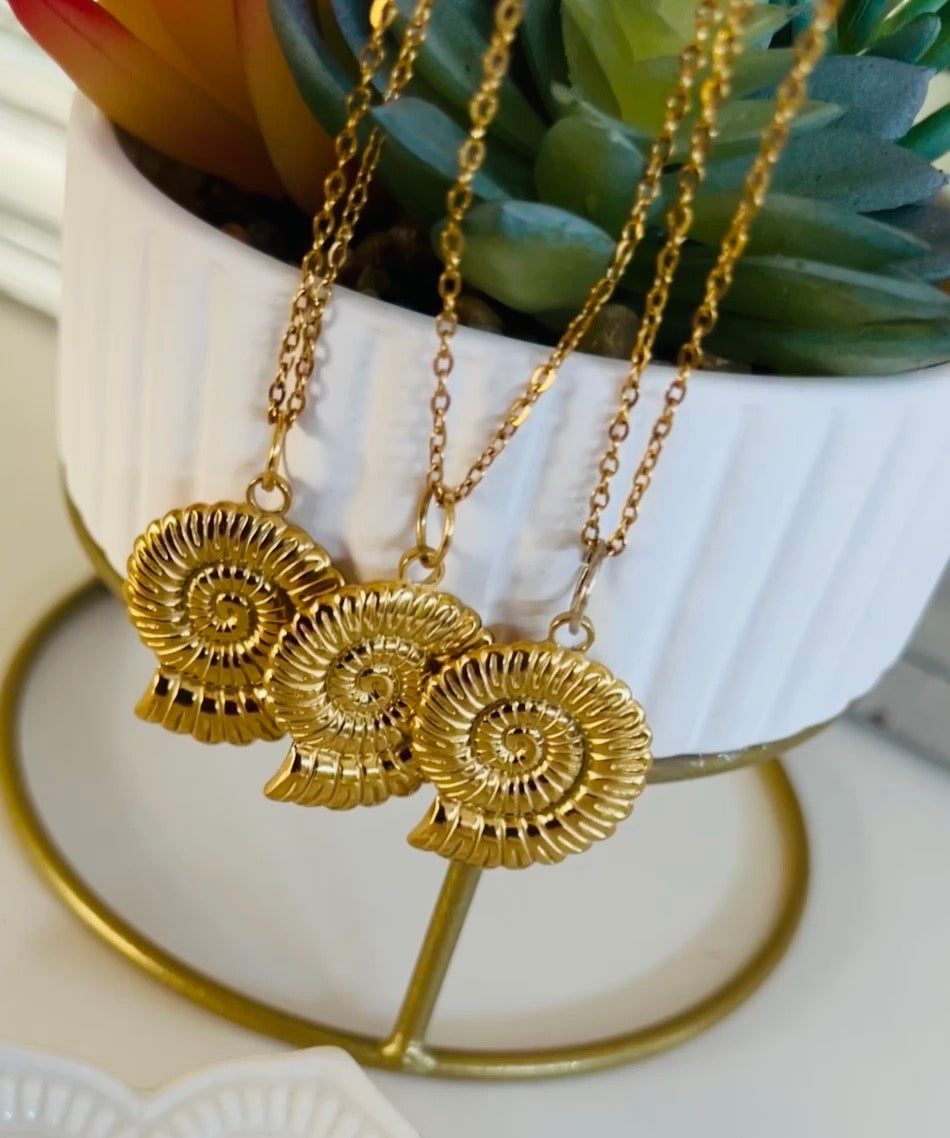 Gold necklaces with decorative pendants on a white stand with a plant in the background