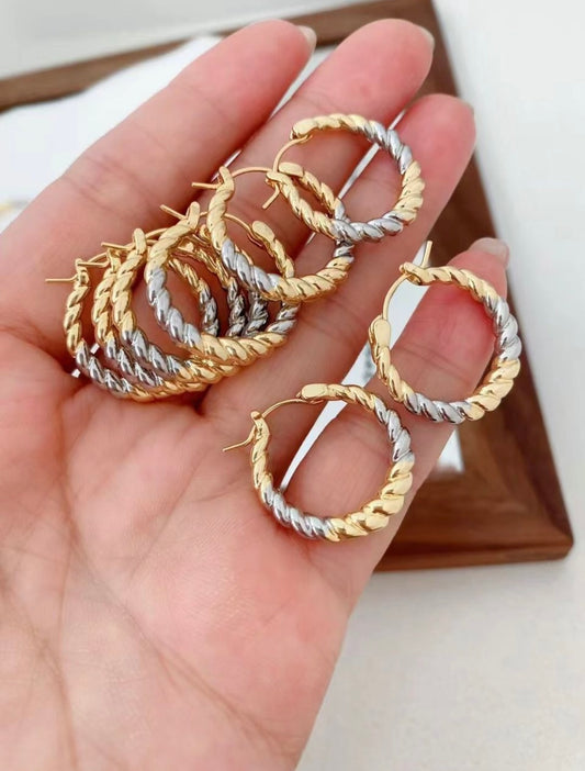 Gold and silver hoop earrings held in a hand with a neutral background