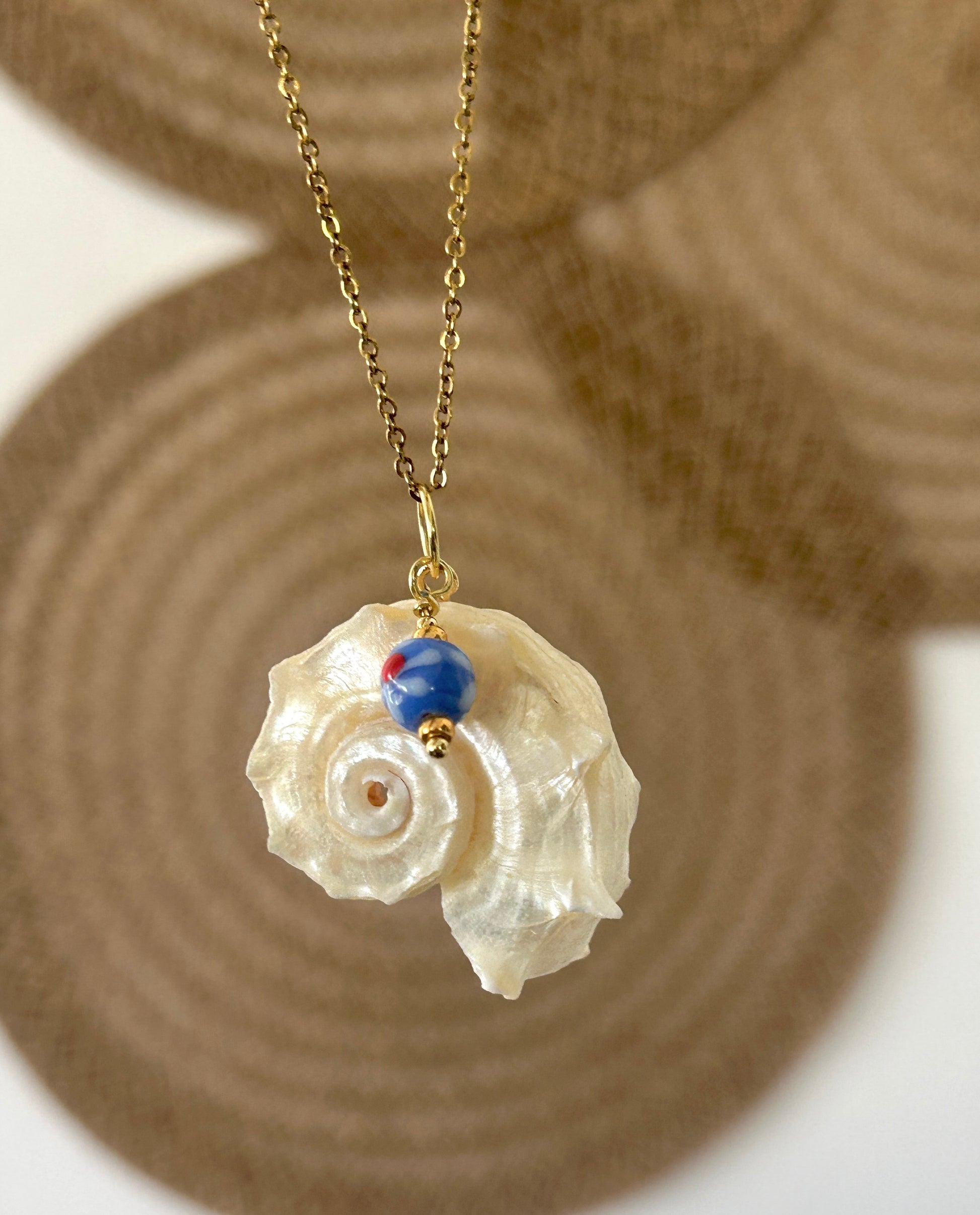 Necklace with a shell pendant and blue bead on a textured surface
