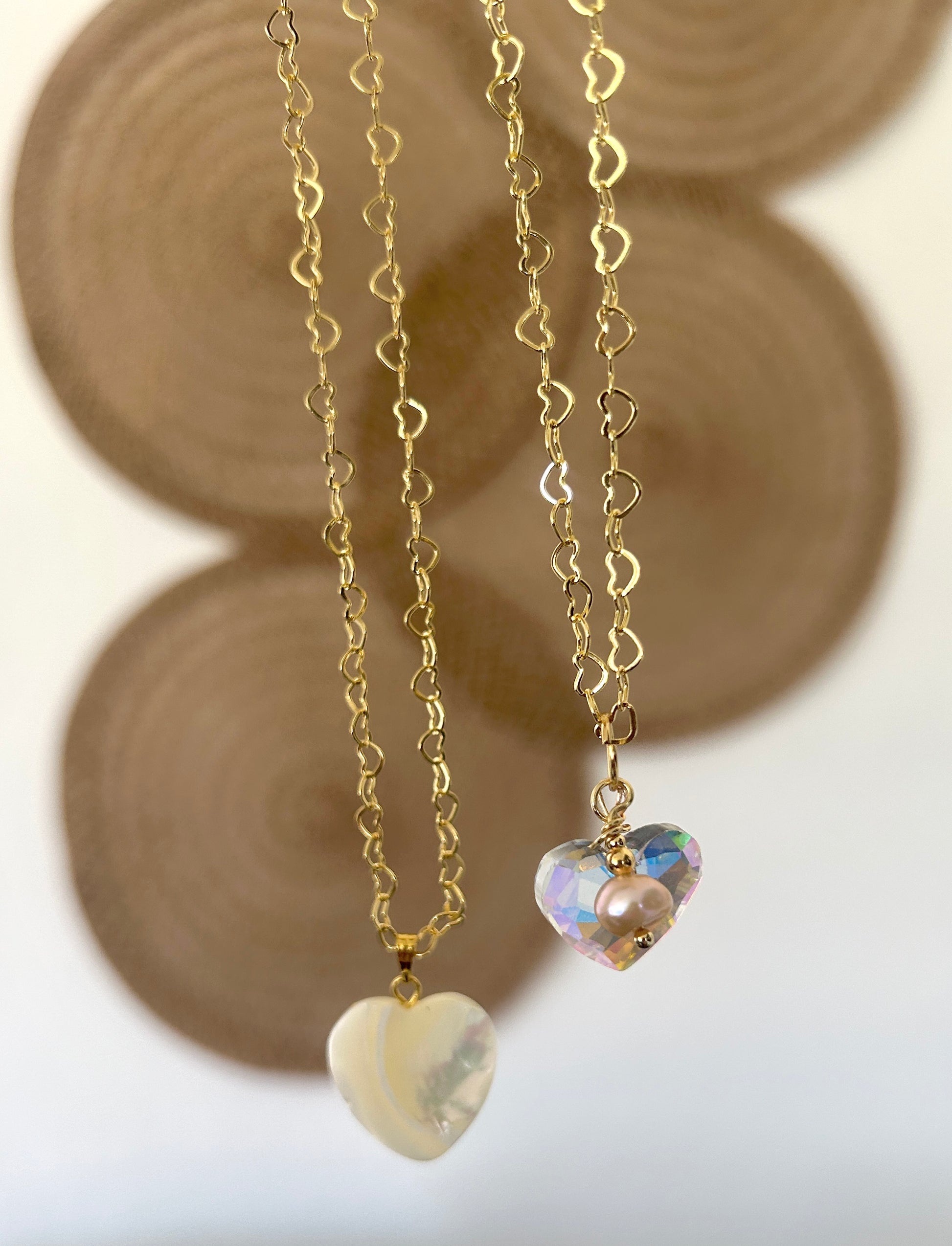 Two heart-shaped pendants on gold chains with a blurred background