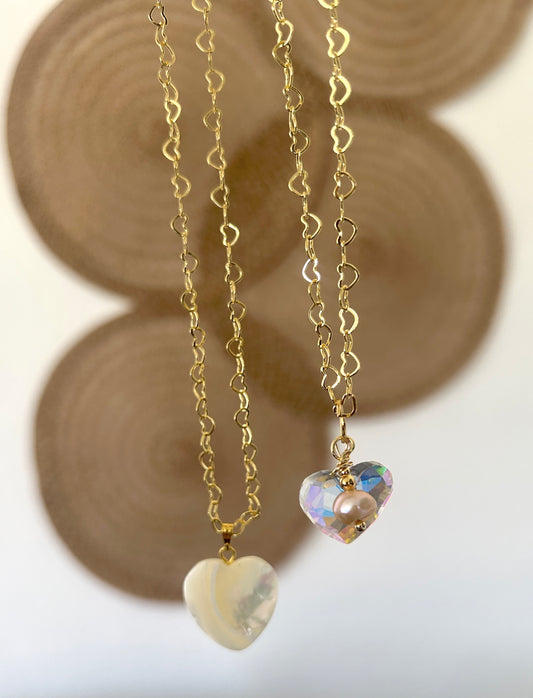 Two heart-shaped pendants on gold chains with a blurred background