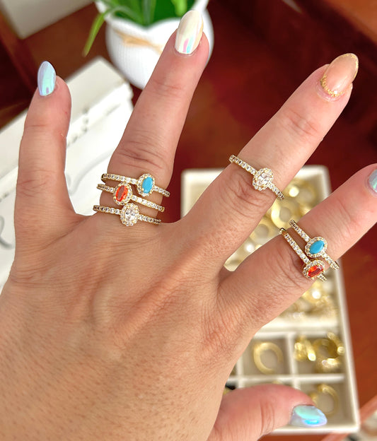 Hand wearing two rings with gemstones on a blurred indoor background