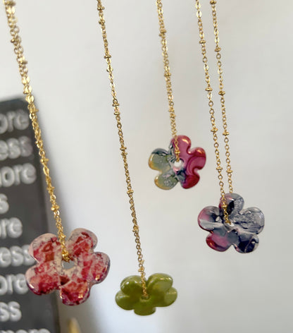 Three floral pendant necklaces on gold chains with a blurred background.