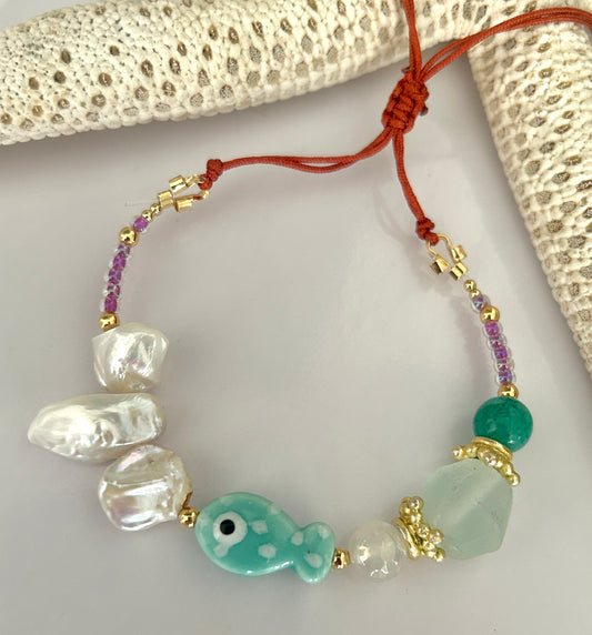 Beaded bracelet with fish charm on a textured surface