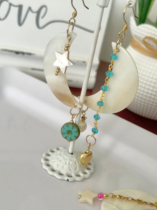 Earrings with star and floral charms on a decorative stand with a shell background.