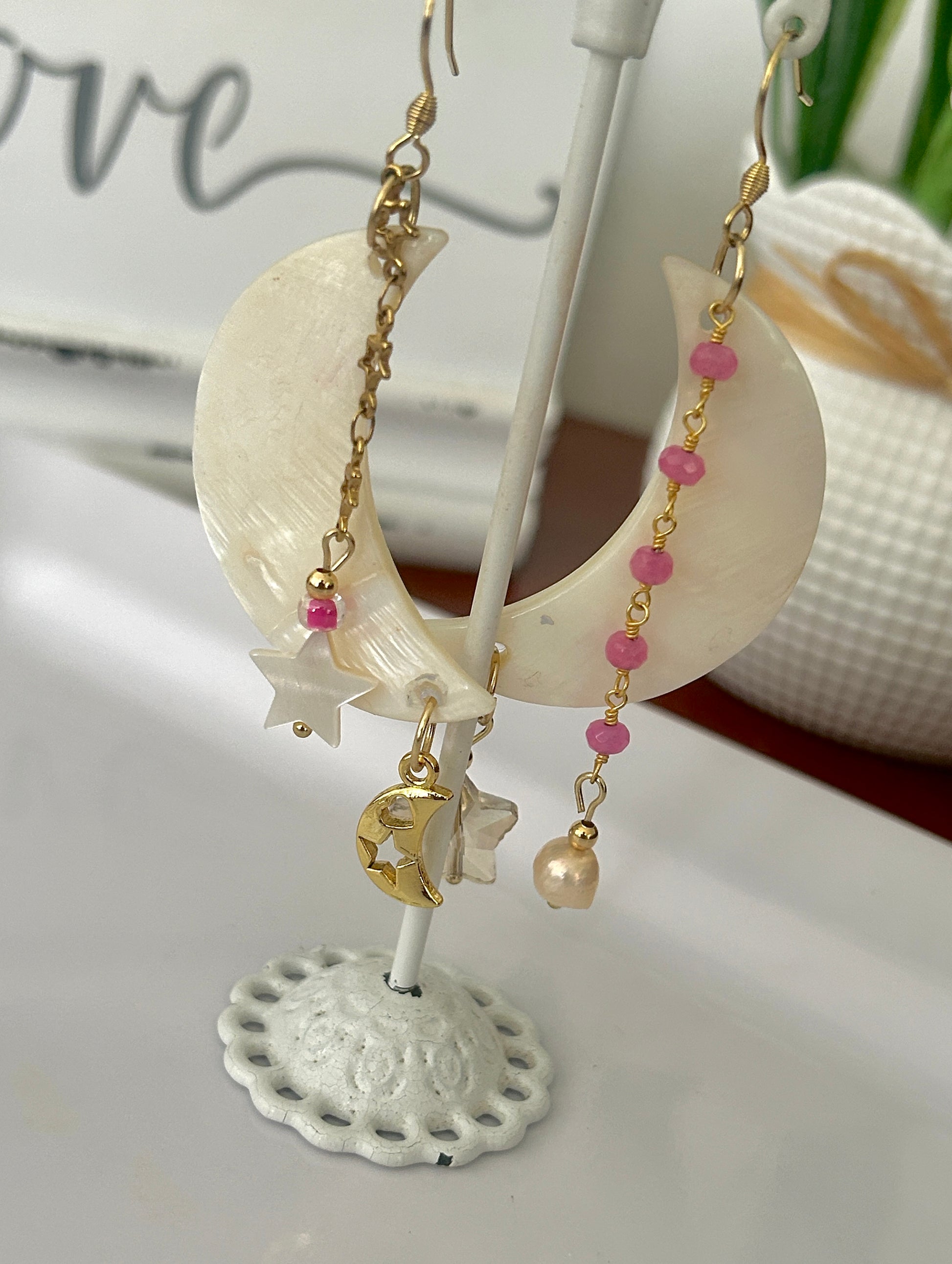 Shell earrings with pink beads and gold accents on a decorative stand.