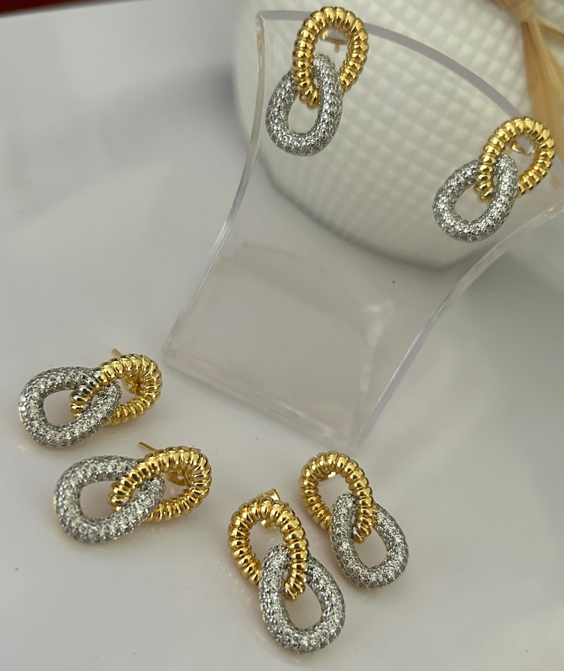 Gold and silver interlinked earrings on a white surface with a clear stand.