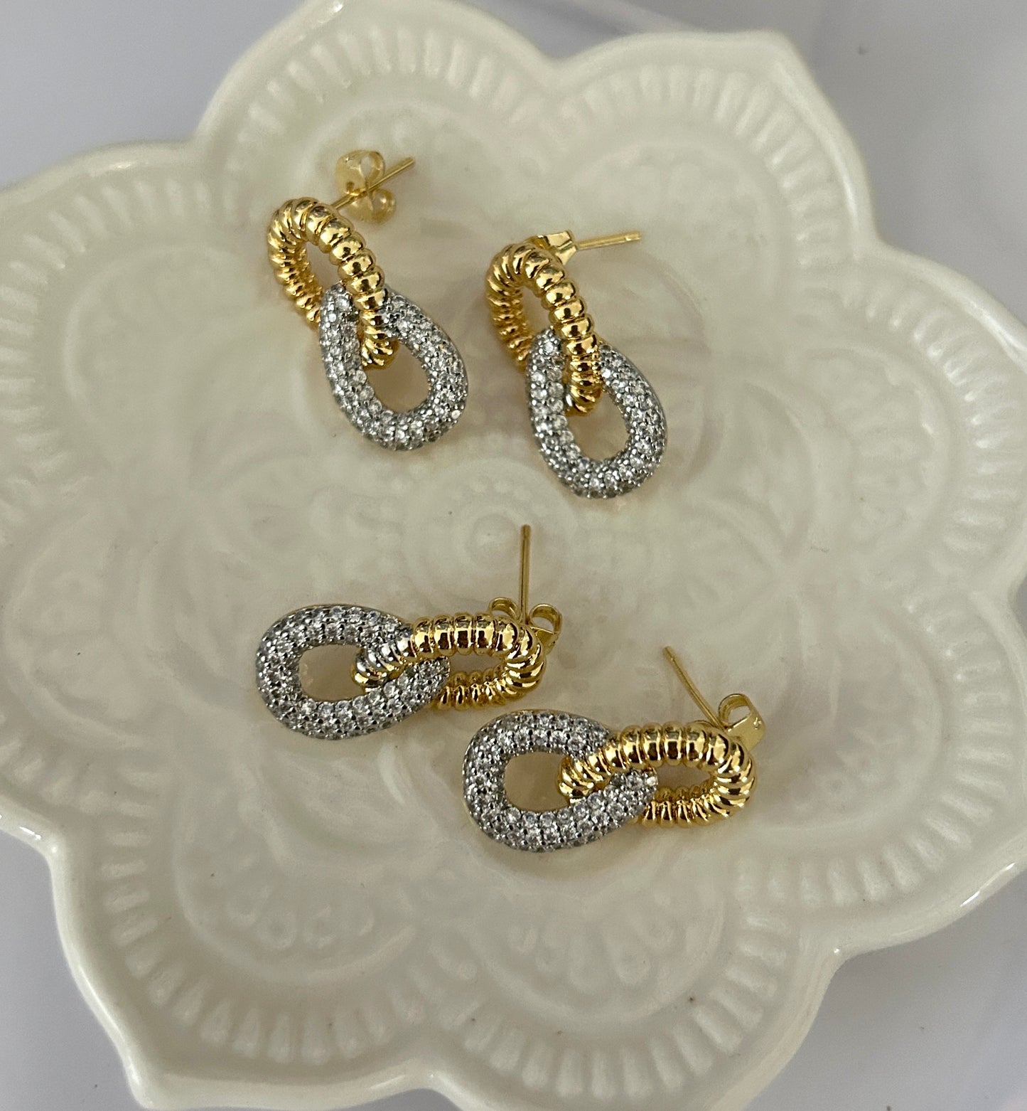 Pair of gold and silver hoop earrings on a decorative white dish.