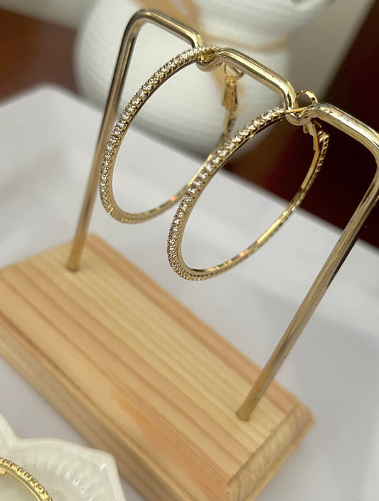 Gold hoop earrings on a wooden stand with a blurred background