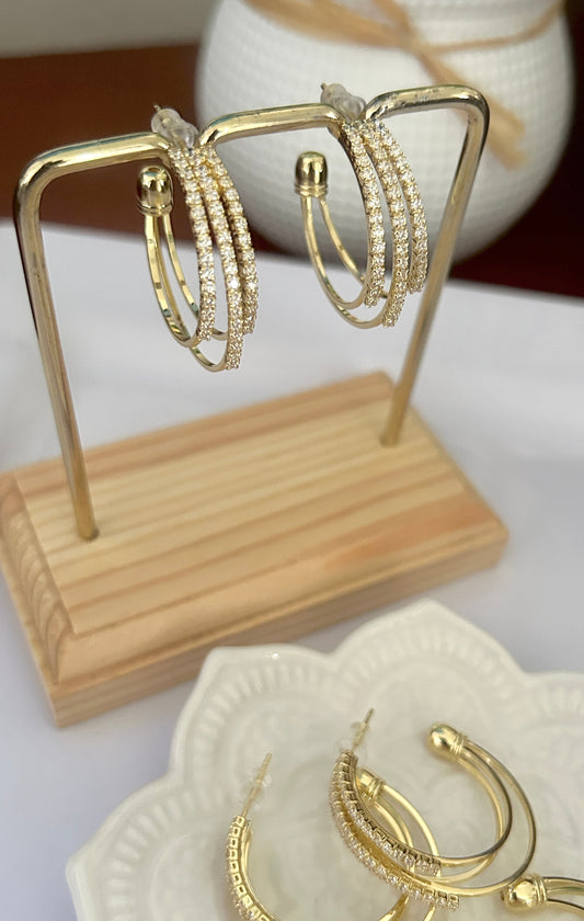 Gold hoop earrings on a wooden stand with additional earrings on a white dish.