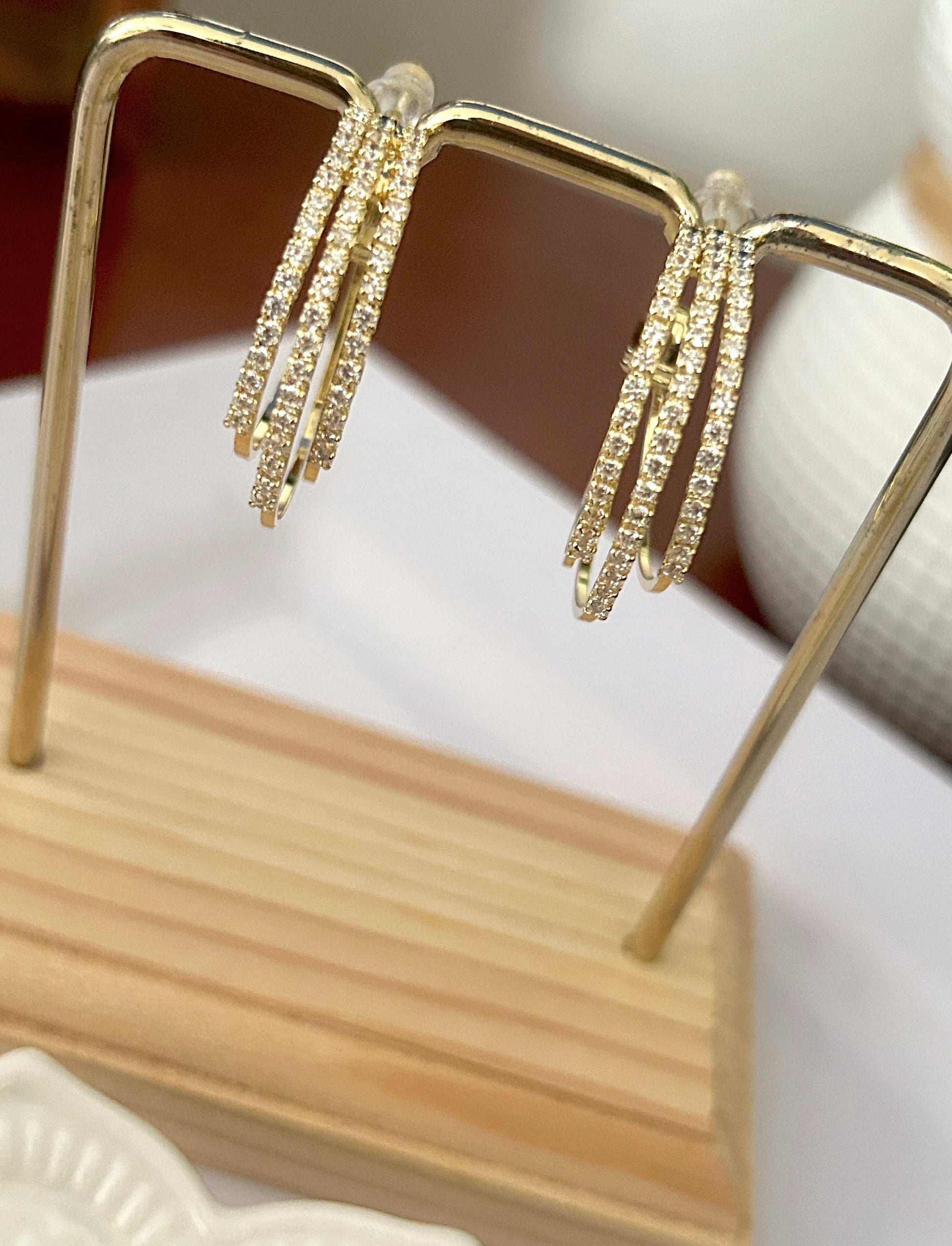 Gold hoop earrings on a wooden stand with a blurred background