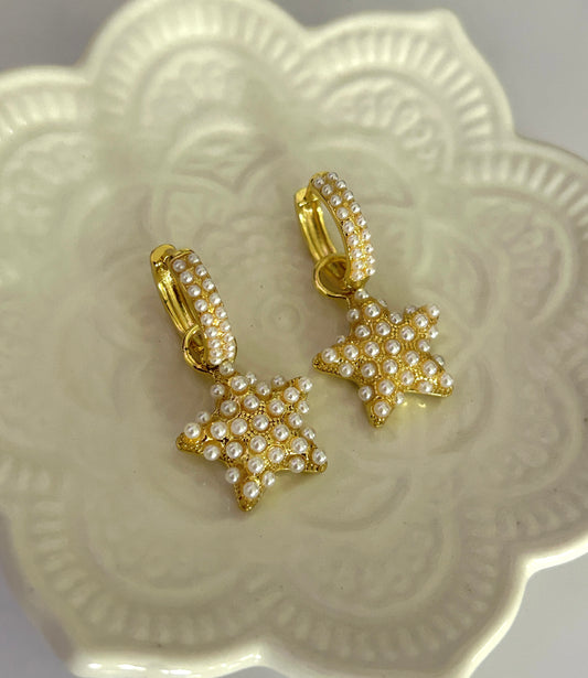 Gold star-shaped earrings with pearl details on a decorative white plate.
