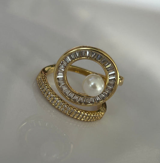 Gold ring with pearl and gemstones on a reflective surface